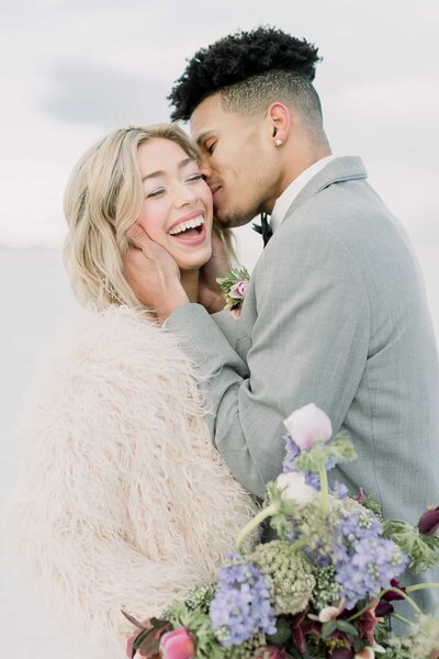 A groom kisses his bride on the cheek while at the Bonneville Salt Flats on their wedding day. 
