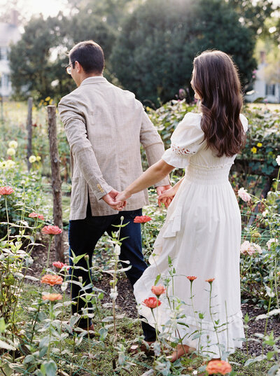  Couple walking hand-in-hand through floral garden, captured by a Fine Art Wedding Photographer Seattle for editorial engagement sessions.