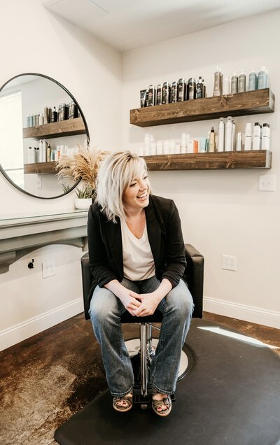 Sara Carter, founder and stylist at Maven + Grace Salon, smiling and seated in her light-filled studio space in McMinnville