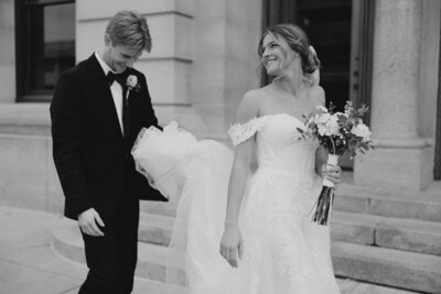 Bride and groom walking after their wedding ceremony in black and white, groom is holding the brides dress so it doesn't drag on the ground