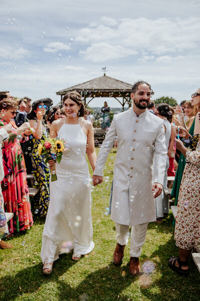 Bride and groom walk through a flurry of multicoloured confetti at King's Chapel, Amersham