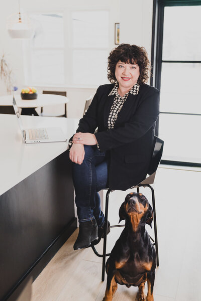 Desiree Peterson on a corporate attire sitting on her office with her dog