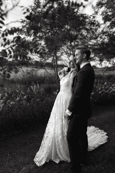 A bride relaxes against the shoulder of a groom wearing a tuxedo during a golden hour moment in Prince edward county with the wedding taking place at brighthouse farm