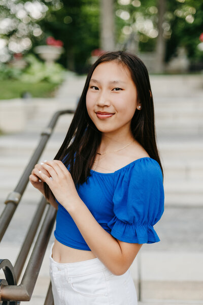 Senior girl in a blue top and white pants twirling her hair in her fingers