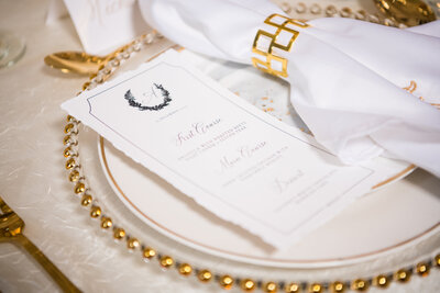 Chic wedding reception table setting featuring a gold-rimmed charger and custom menu card for a luxury event.