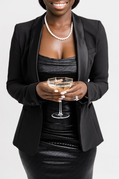 designer in all black with pearls holding glass of champagne