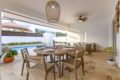 Covered patio with a large dining table and pool view at a luxury property by Nova Lux DR Properties