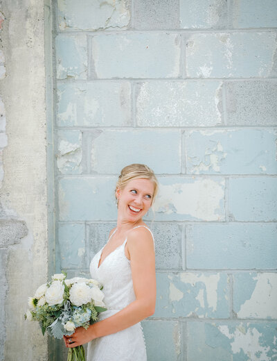 A bride by a blue brick wall looking at her groom with a Grand Rapids wedding photographer