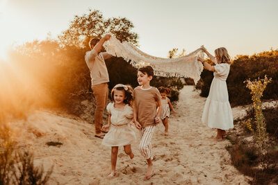 Playful family photo session at sunset in Laguna Niguel with kids running under a blanket
