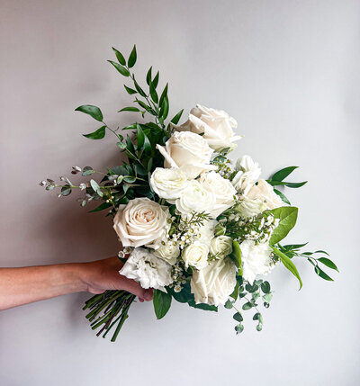 Arm holding a white floral bouquet with greenery
