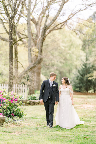Bride and groom take a romantic walk through a lush garden in spring, surrounded by vibrant flowers and fresh greenery, embracing the beauty of their wedding day.