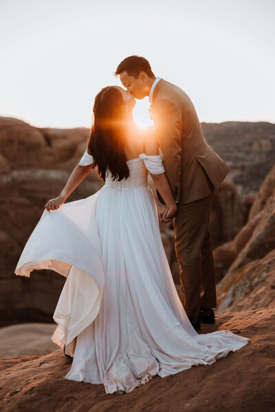 bride and groom kissing while standing on large rock formation in the desert