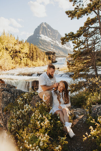 Couple posing on rocks near river waterfalls in Glacier National Park during an adventurous elopement.