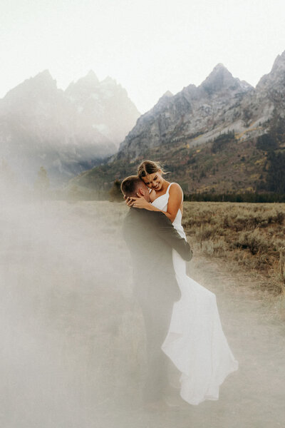 photo of bride and groom embracing while standing outside with mountains in the background