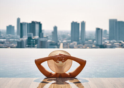 Woman wearing a hat with her hands on her head in a rooftop pool overlooking the city