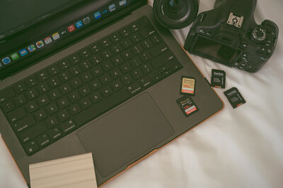 A detail shot of Michaela's open laptop with four SD cards, her camera, and a lens lying next to it.