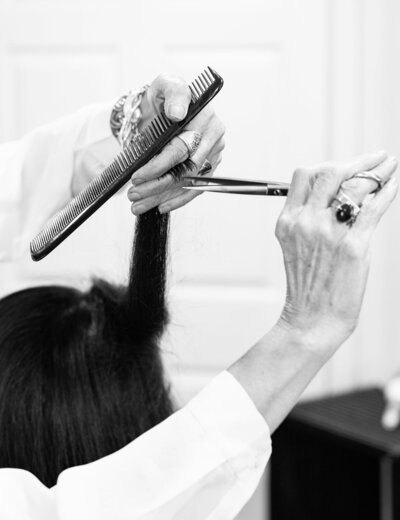 A black and white close-up image showing hands holding professional hairdressing scissors and a comb, poised to work on hair.