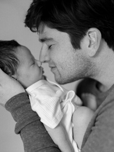 Black and white photo of dad touching noses with his newborn baby