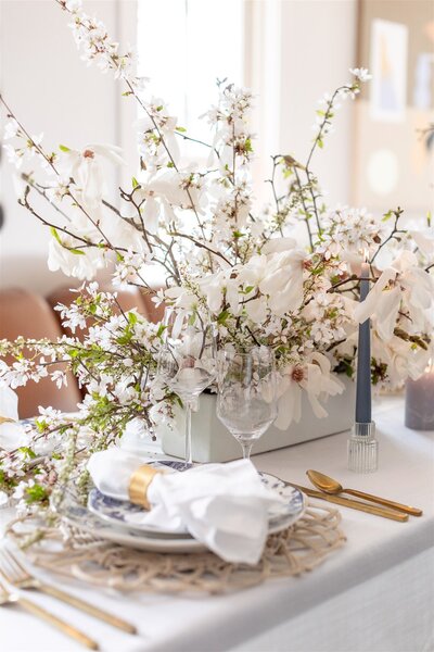A beautifully designed wedding table setting with overflowing white flowers, gold cutlery, and white cloth napkins.