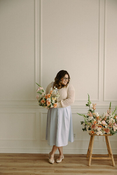 Wedding planner, Zelie & Co., holding a bouquet and looking off to a floral arrangement on a stool