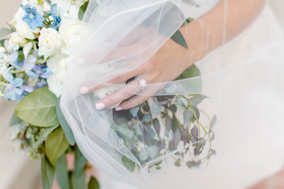 Close up of a brides hand and ring holding her bouquet with the veil