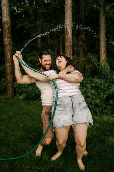 Bryan and Olivia of O & B Photo Co laugh while wresting over a garden hose in their yard. 