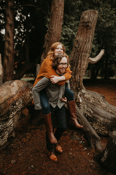Man gives his fiance a piggy back ride while laughing at their engagement photography session at Volunteer Park