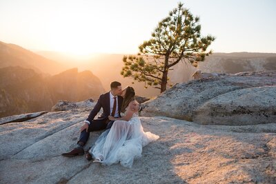 A bride and groom kiss during sunset while sitting on the granite surface rocks at Taft Point.