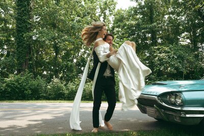 Bride and groom laughing as they run barefoot around a vintage getaway car at their Nashville wedding—captured in dreamy, cinematic light.