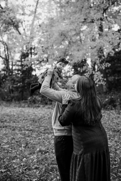 Black and white photo of six month old baby girl being held up by dad and both mom and dad looking at her.