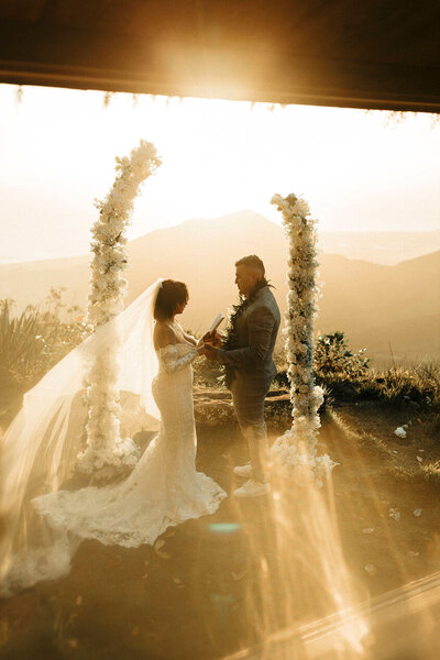 Bride and groom exchanging vows at sunset on a Hawaiian mountaintop — intimate Oahu vow renewal captured by Leslie Carbajal Photography.