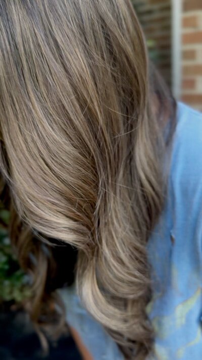 A close-up view of healthy, flowing blonde hair with subtle highlights, styled with soft waves, showcasing a natural and refined look.