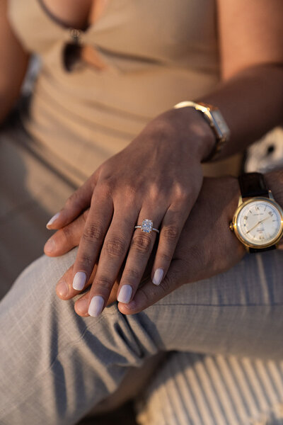 Close-up of an engagement ring on a woman’s hand resting on her partner’s lap