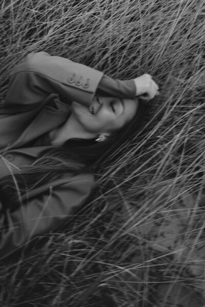 A Michigan photographer laying in dune grass and laughing on a cloudy day. 