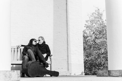 Open Book Music duo Rick and Michele Gedney sitting on bench of The Chapel Restoration in Cold Spring, NY with guitar.