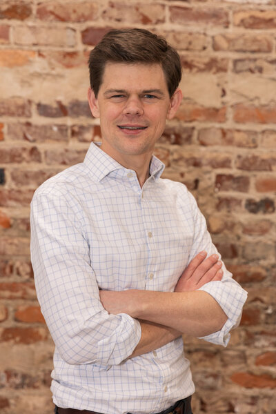 man wearing a long sleeve shirt standing arms crossed in front of a brick wall for headshots Atlanta Brand Photographer