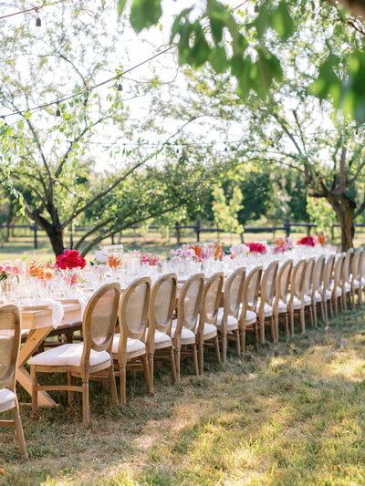 Wedding reception table close up: warm orange, pink and red flowers, scalopped white dishes, and tied white handkerchiefs