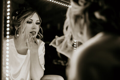 bride looking into a mirror while applying her lipstick as she gets ready for her little rock wedding