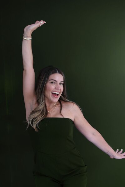 Natalie Bernacchi smiling with her arm raised joyfully in front of a dark green wall, exuding confidence and celebration