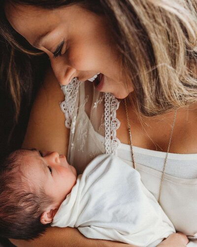 New mom smiles down at her baby girl during a lifestyle newborn photo session in Pittsburgh