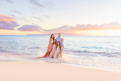 family dips their toes in the water as the tide moves up the beach in Maui during their family photo session