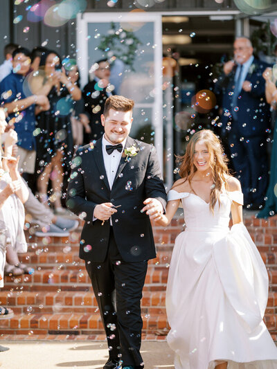 bride and groom hold hands and smile during bubble exit in Central Arkansas