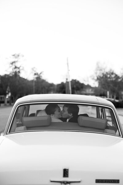 Bride and groom kiss through the back of the vintage car window
