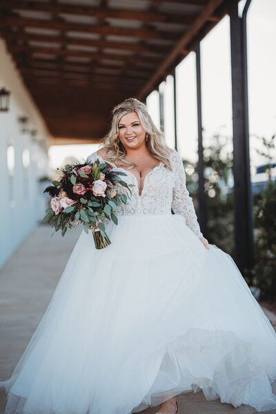 Bride in a lace long-sleeve ball gown holding a bouquet while walking outdoors