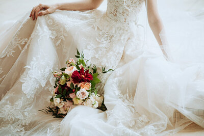 Detail close up of bride holding her flowing dress with bouquet sitting in her lap