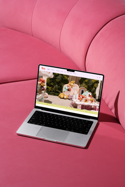 A laptop computer sitting on a pink couch. The laptop is a silver MacBook Pro and it is closed.  There is a black and white patterned throw blanket folded in half on the right side of the couch.