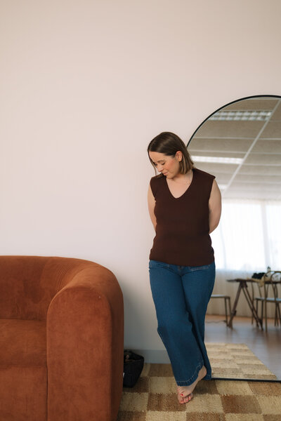 Liv Rollings posing by tall mirror and rust colored couch