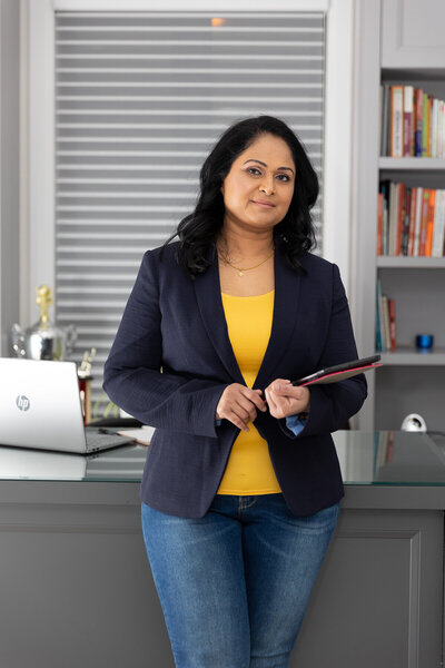 Kalinie holding an ipad standing in front of a desk with a laptop on it.