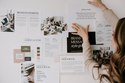 Website copywriter Erika Fitzgerald taping brand positioning documents, including messaging, client avatars, audience research, and wireframes, to a wall as part of a website copywriting process