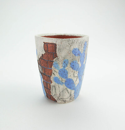 A ceramic cup that resembles plaster falling apart from red bricks with painted cacti and graffiti